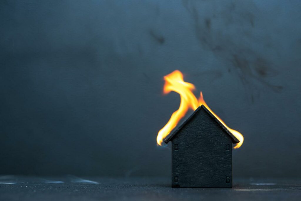 Black little wooden house caught fire on dark background.
